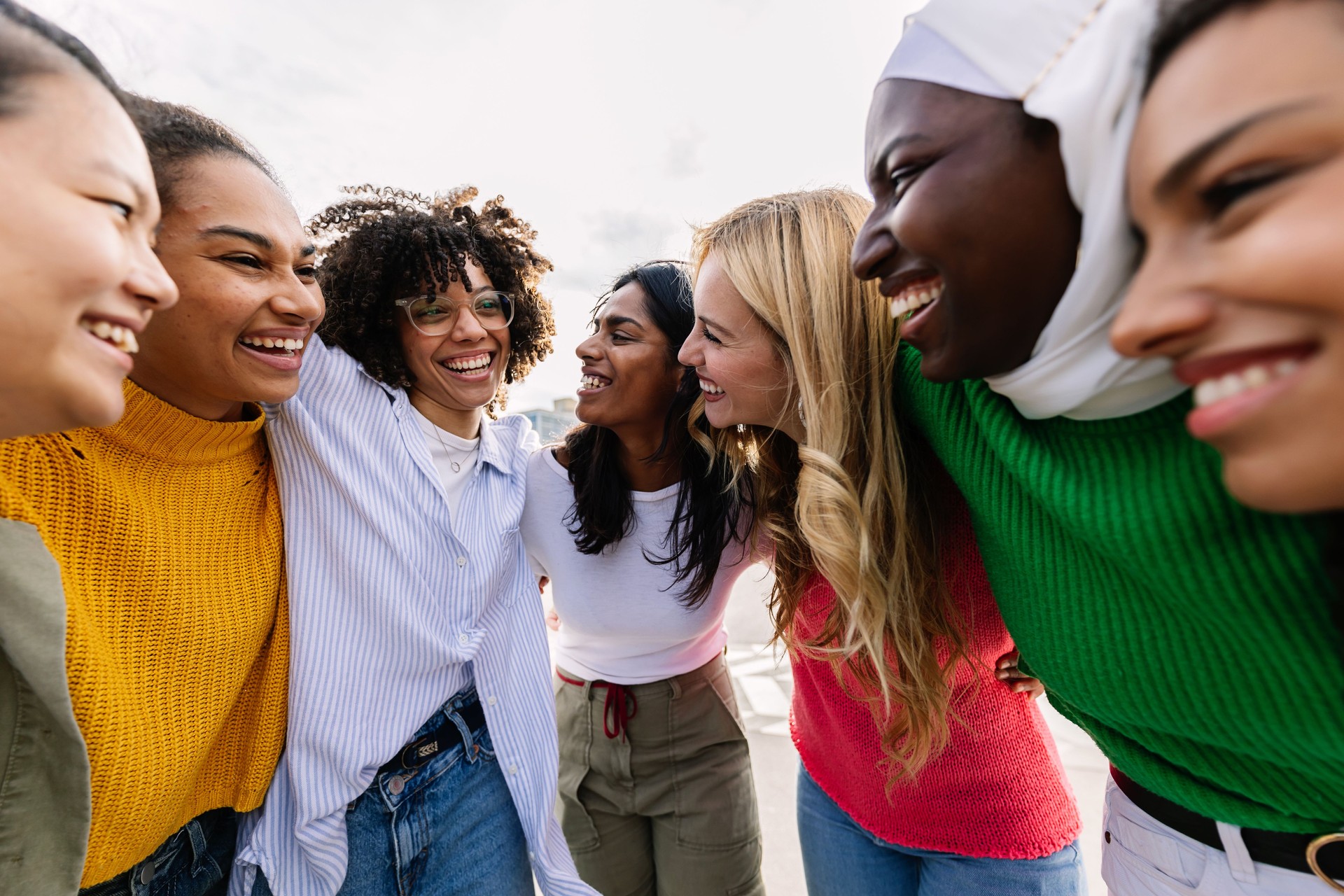 Sept jeunes femmes adultes heureuses de différentes cultures riant ensemble à l’extérieur